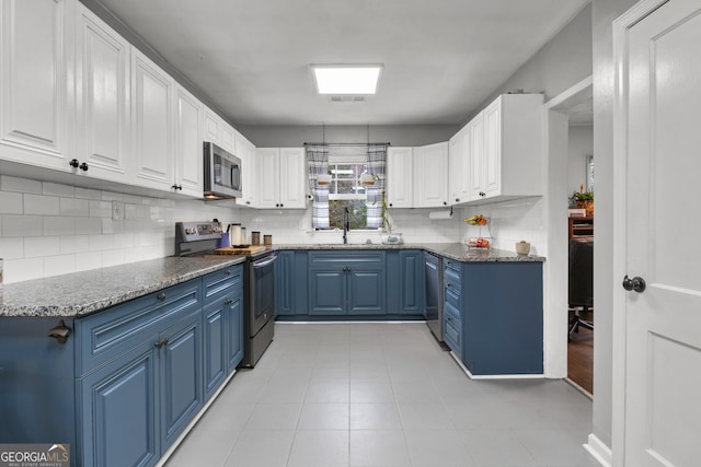 kitchen with appliances with stainless steel finishes, blue cabinets, sink, white cabinets, and dark stone counters