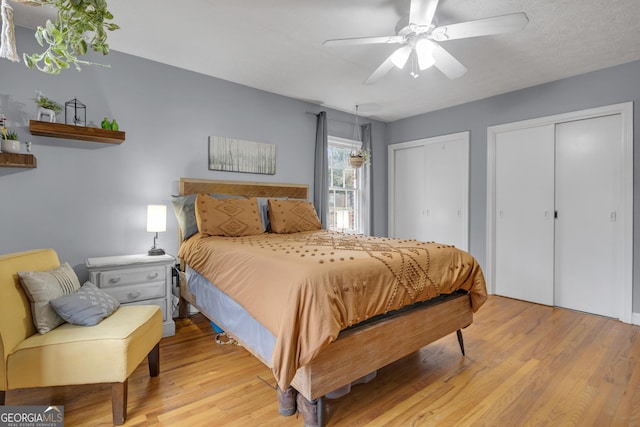 bedroom with ceiling fan, light hardwood / wood-style flooring, and multiple closets