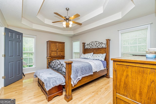 bedroom featuring ceiling fan, a tray ceiling, and light hardwood / wood-style floors