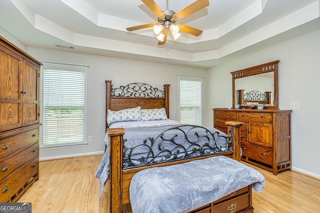 bedroom with ceiling fan, a tray ceiling, and light hardwood / wood-style floors