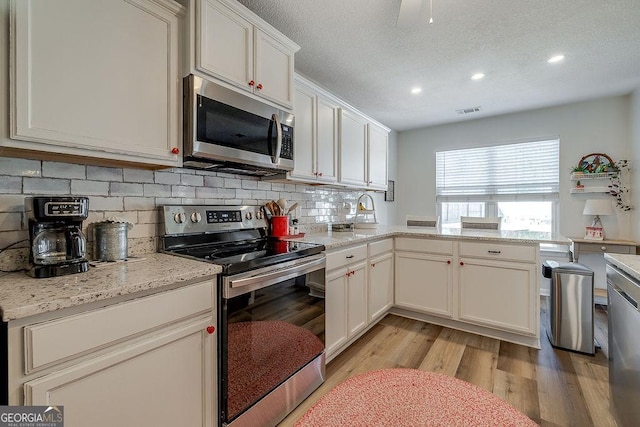 kitchen with light stone counters, stainless steel appliances, light hardwood / wood-style flooring, and white cabinets