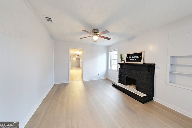 living room with a stone fireplace, ceiling fan, light hardwood / wood-style floors, a textured ceiling, and built in shelves