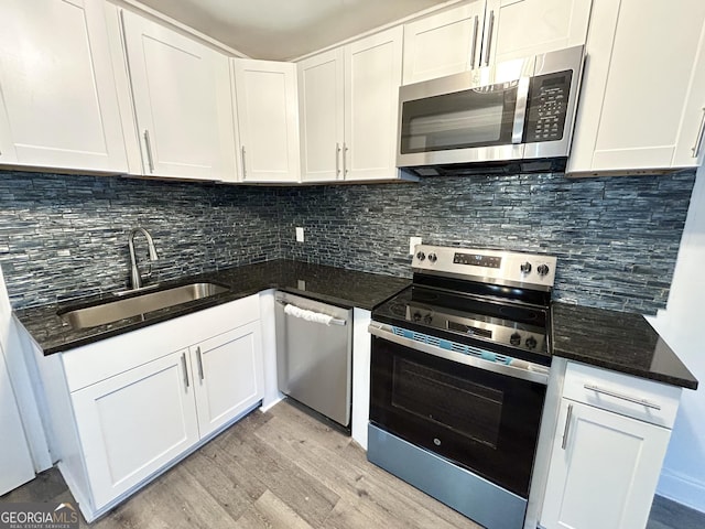 kitchen with sink, appliances with stainless steel finishes, white cabinetry, light hardwood / wood-style floors, and decorative backsplash