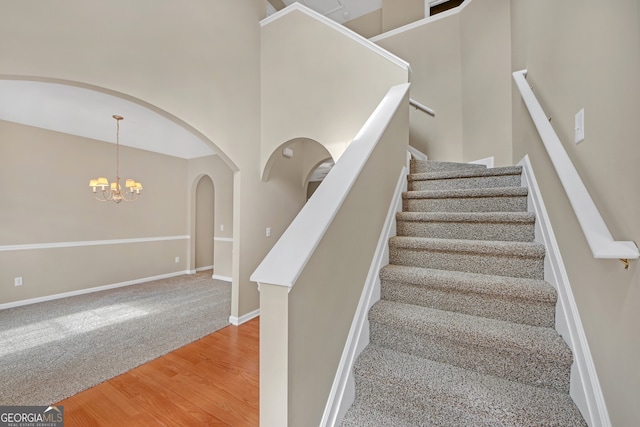 stairway with hardwood / wood-style flooring, a towering ceiling, and a notable chandelier