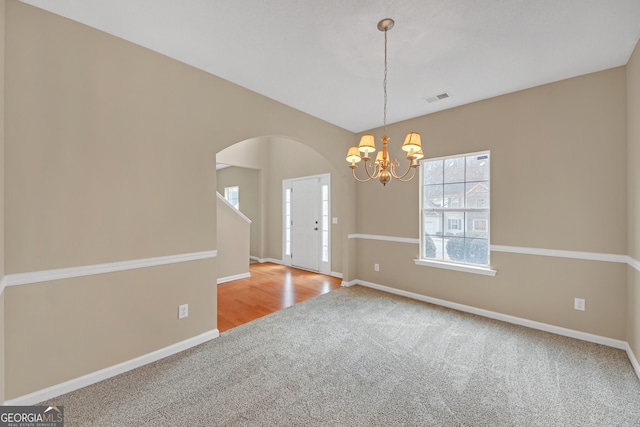 carpeted empty room with an inviting chandelier