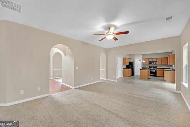 unfurnished living room with ceiling fan, light colored carpet, and a textured ceiling