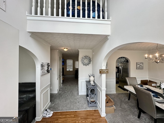 hall with crown molding, an inviting chandelier, a textured ceiling, a towering ceiling, and hardwood / wood-style floors