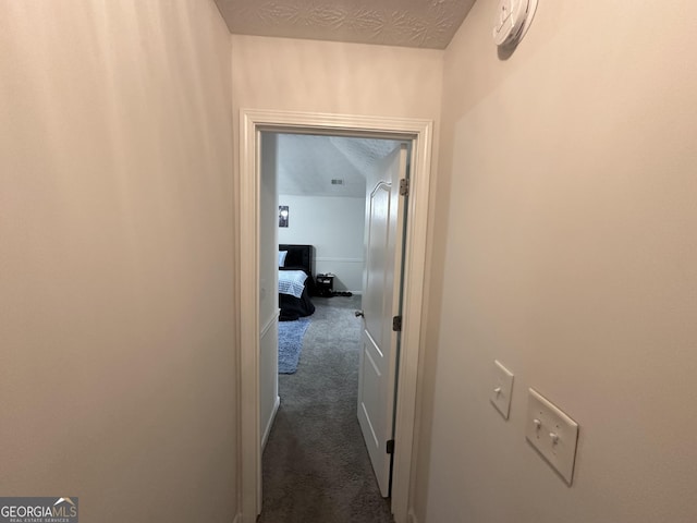 hallway with dark colored carpet and a textured ceiling