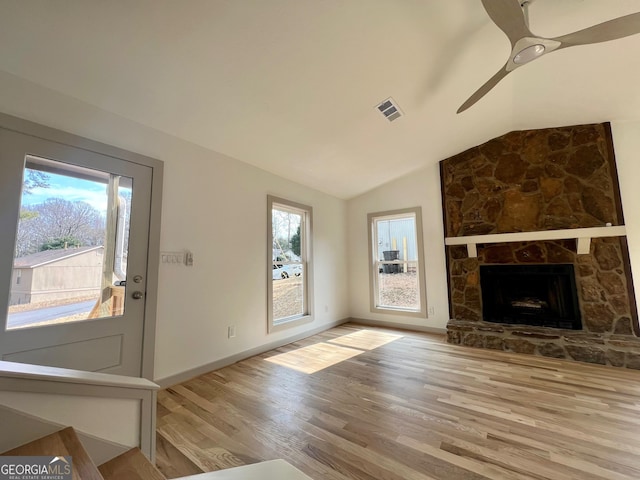 unfurnished living room featuring vaulted ceiling, a stone fireplace, ceiling fan, and light hardwood / wood-style flooring