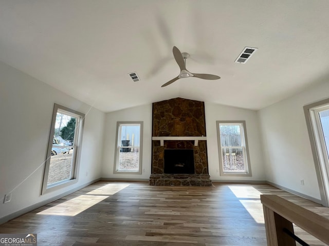 unfurnished living room featuring lofted ceiling, a stone fireplace, wood-type flooring, and a healthy amount of sunlight