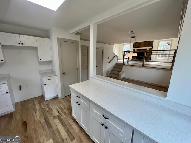 kitchen with light hardwood / wood-style flooring, light stone countertops, hanging light fixtures, and white cabinets