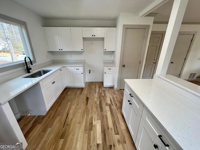 kitchen featuring white cabinetry, sink, light stone counters, and light wood-type flooring