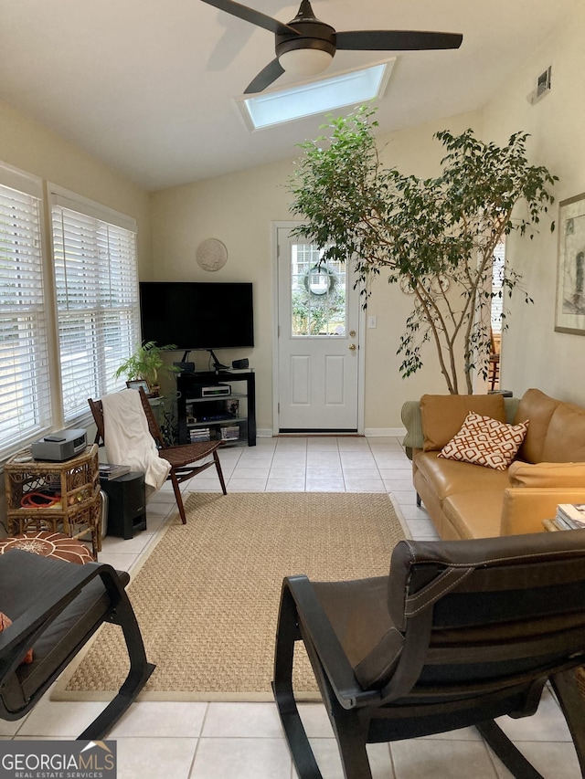 living room with ceiling fan, a healthy amount of sunlight, lofted ceiling with skylight, and light tile patterned floors