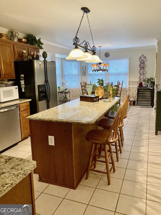 kitchen featuring a kitchen island, decorative light fixtures, ornamental molding, light tile patterned floors, and stainless steel appliances