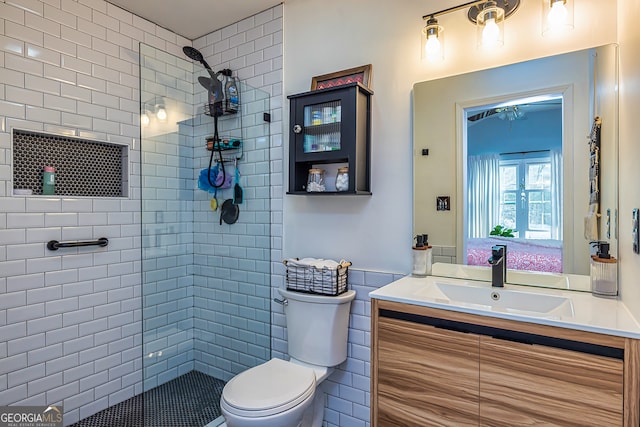 bathroom with tiled shower, vanity, toilet, and tile walls