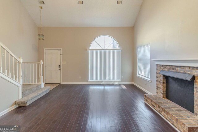 unfurnished living room with dark hardwood / wood-style flooring, a brick fireplace, and high vaulted ceiling