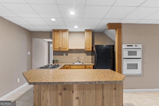 kitchen featuring sink, black refrigerator, double oven, light tile patterned flooring, and stainless steel gas stovetop