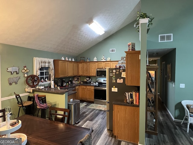 kitchen with dark hardwood / wood-style floors, high vaulted ceiling, kitchen peninsula, stainless steel appliances, and a textured ceiling