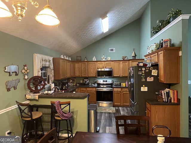 kitchen with a kitchen bar, decorative light fixtures, appliances with stainless steel finishes, dark hardwood / wood-style flooring, and kitchen peninsula