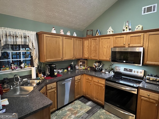 kitchen with appliances with stainless steel finishes, hardwood / wood-style floors, lofted ceiling, sink, and a textured ceiling