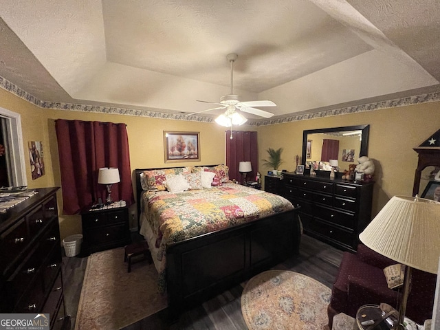 bedroom with ceiling fan, a tray ceiling, dark hardwood / wood-style flooring, and a textured ceiling