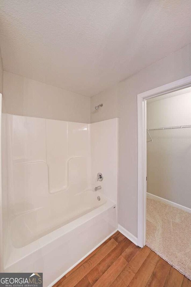 bathroom with wood-type flooring,  shower combination, and a textured ceiling