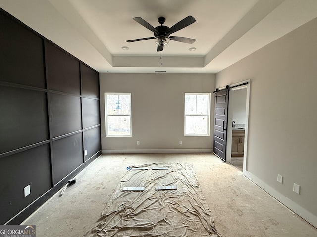 unfurnished bedroom with a barn door, multiple windows, baseboards, and a raised ceiling