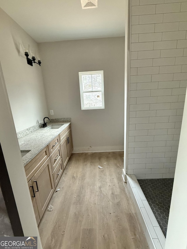 bathroom with a tile shower, double vanity, wood finished floors, and a sink