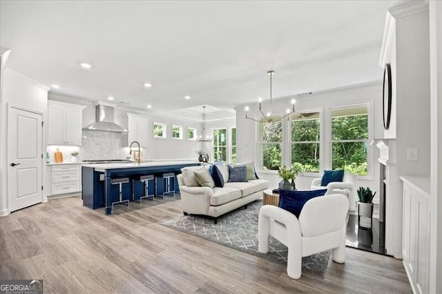 living room with ornamental molding, sink, light wood-type flooring, and a notable chandelier