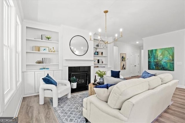 living room with crown molding, an inviting chandelier, light hardwood / wood-style floors, and built in shelves