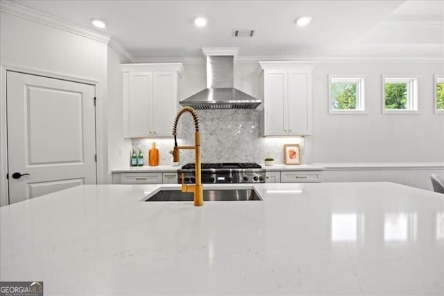 kitchen with wall chimney range hood, crown molding, light stone countertops, and white cabinets