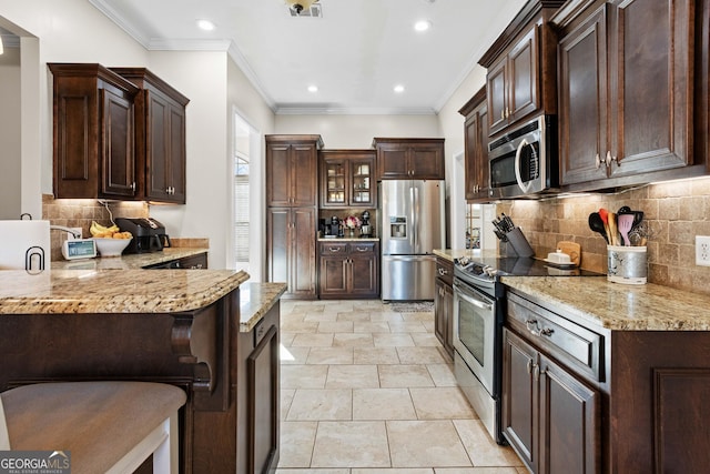 kitchen with light stone counters, dark brown cabinetry, a kitchen breakfast bar, and appliances with stainless steel finishes