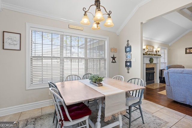 tiled dining area featuring a tile fireplace, lofted ceiling, ornamental molding, and an inviting chandelier