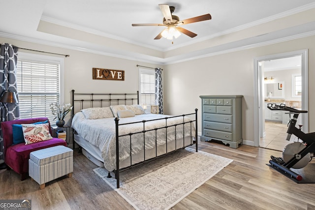 bedroom with wood-type flooring, ornamental molding, connected bathroom, and a tray ceiling