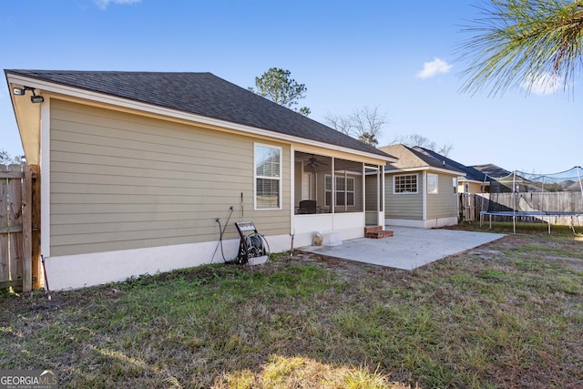 back of house featuring a patio, a yard, a sunroom, and a trampoline