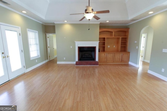 unfurnished living room with crown molding, light hardwood / wood-style flooring, a tray ceiling, ceiling fan, and a fireplace