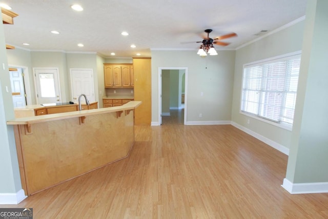 kitchen with sink, crown molding, a kitchen bar, light brown cabinetry, and light wood-type flooring