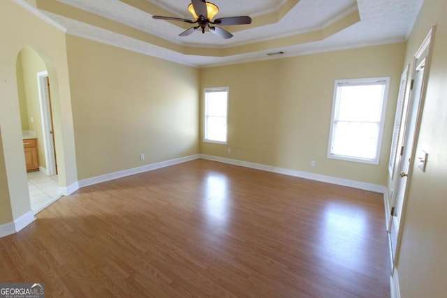 unfurnished room featuring a tray ceiling, ornamental molding, light hardwood / wood-style floors, and ceiling fan