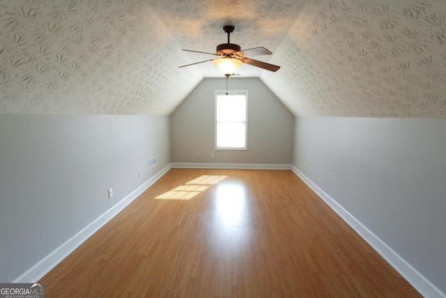 bonus room with wood-type flooring, vaulted ceiling, and a textured ceiling