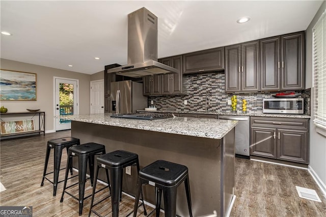 kitchen with island exhaust hood, stainless steel appliances, a center island, and a breakfast bar