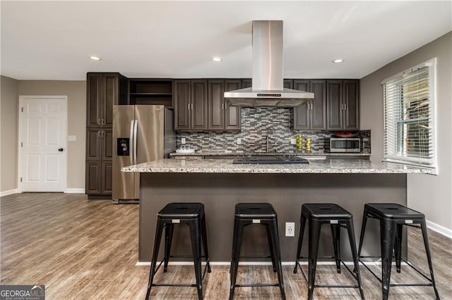 kitchen with hardwood / wood-style flooring, appliances with stainless steel finishes, a kitchen breakfast bar, dark brown cabinetry, and island range hood