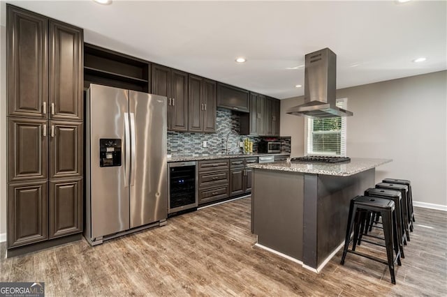 kitchen with wine cooler, a kitchen bar, hardwood / wood-style flooring, island exhaust hood, and stainless steel appliances