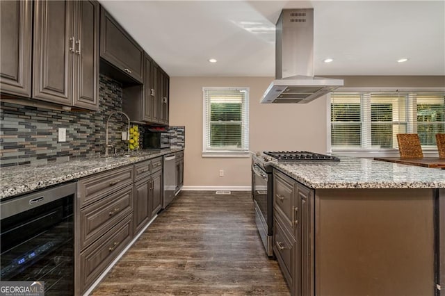 kitchen featuring wine cooler, sink, light stone counters, island range hood, and appliances with stainless steel finishes