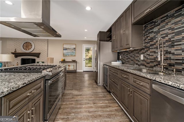 kitchen featuring dark brown cabinetry, sink, island range hood, appliances with stainless steel finishes, and light stone countertops