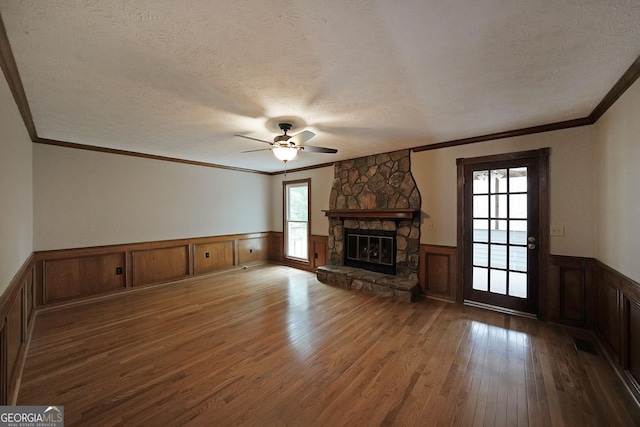 unfurnished living room featuring hardwood / wood-style floors, a stone fireplace, ornamental molding, and a textured ceiling