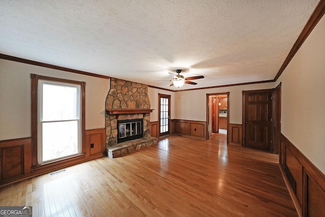 unfurnished living room with wood-type flooring, a textured ceiling, ornamental molding, ceiling fan, and a fireplace