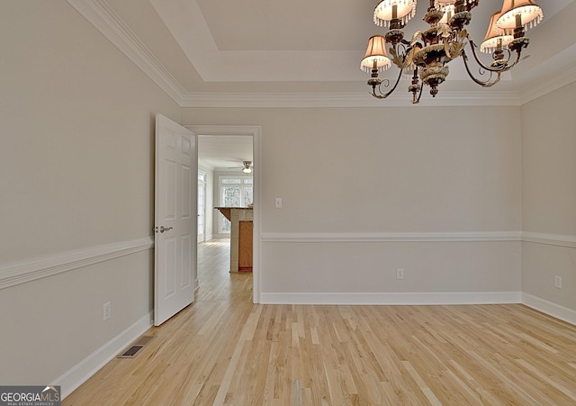 spare room with an inviting chandelier, ornamental molding, a tray ceiling, and light hardwood / wood-style flooring