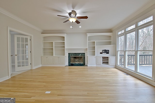 unfurnished living room featuring crown molding, built in features, ceiling fan, a high end fireplace, and light wood-type flooring