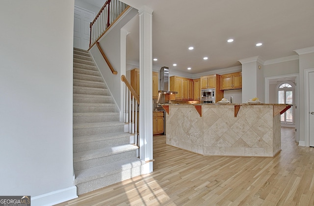 kitchen with stainless steel microwave, wall chimney range hood, light hardwood / wood-style flooring, and a kitchen bar