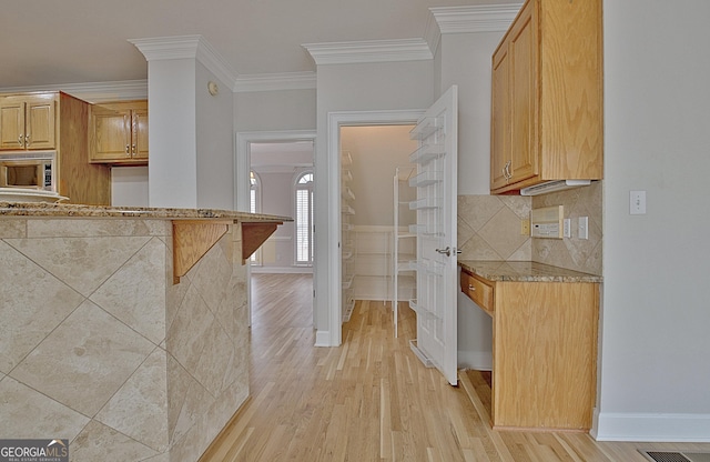 kitchen with backsplash, ornamental molding, a kitchen breakfast bar, and light hardwood / wood-style floors